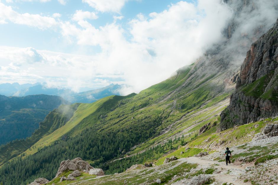 A hiker explores the lush trails of the Dolomite mountains surrounded by clouds.